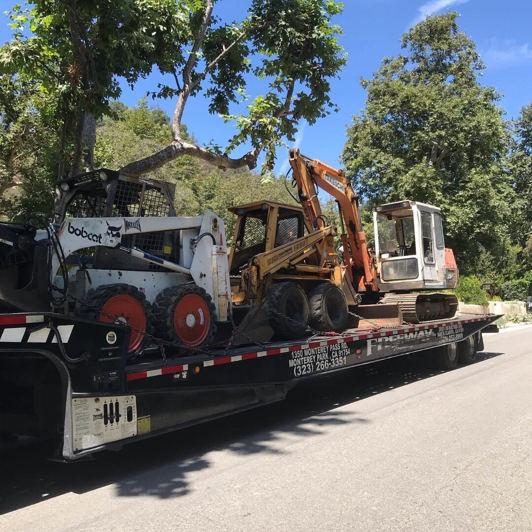 Sierra Development's excavation fleet — two Bobcat skid steers and a Takeuchi mini excavator loaded on a flatbed trailer bound for a jobsite.