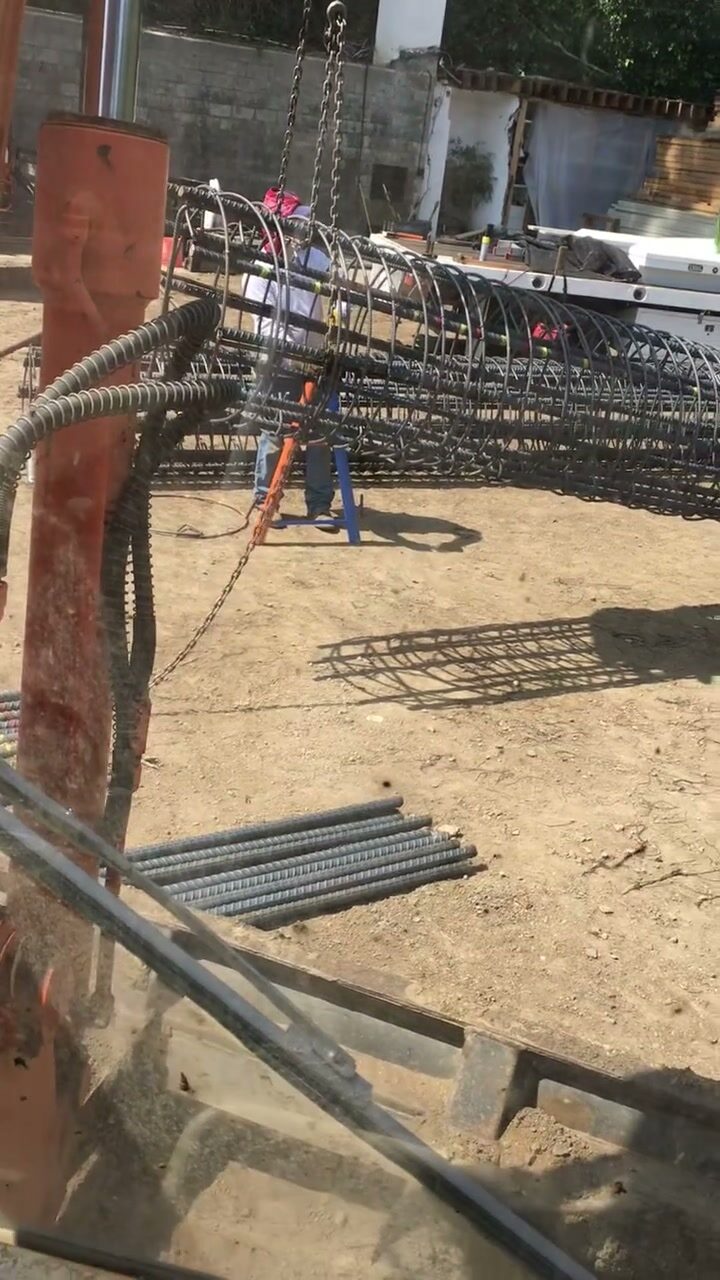 A Sierra Development crew member guiding a large cylindrical rebar cage into position for a retaining wall footing.