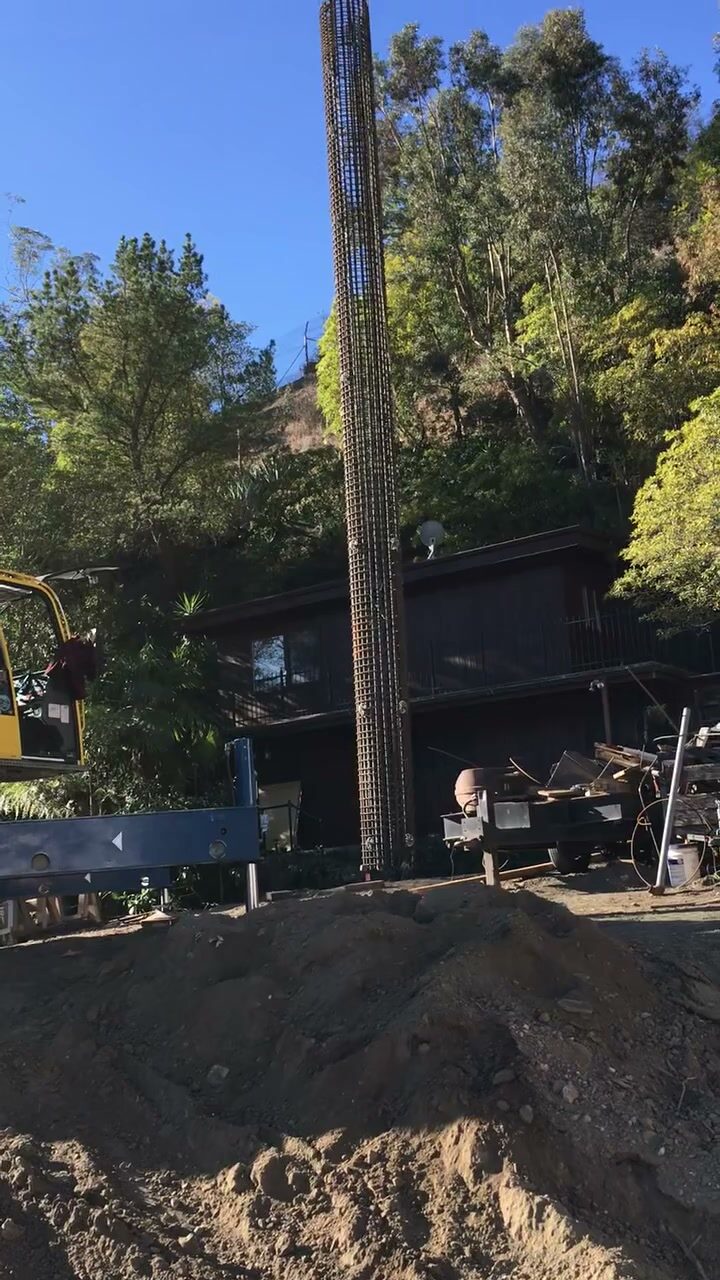 A tall rebar cage installed for a deep foundation pile on a wooded hillside jobsite.